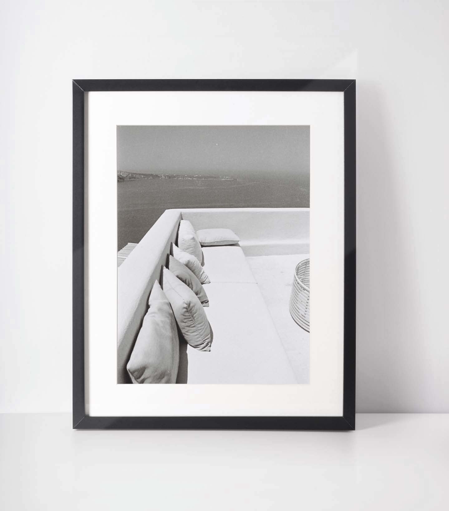 A framed Photograph showing a corner sofa in santorini during an afternoon summer. The view is of the Aegean Sea
